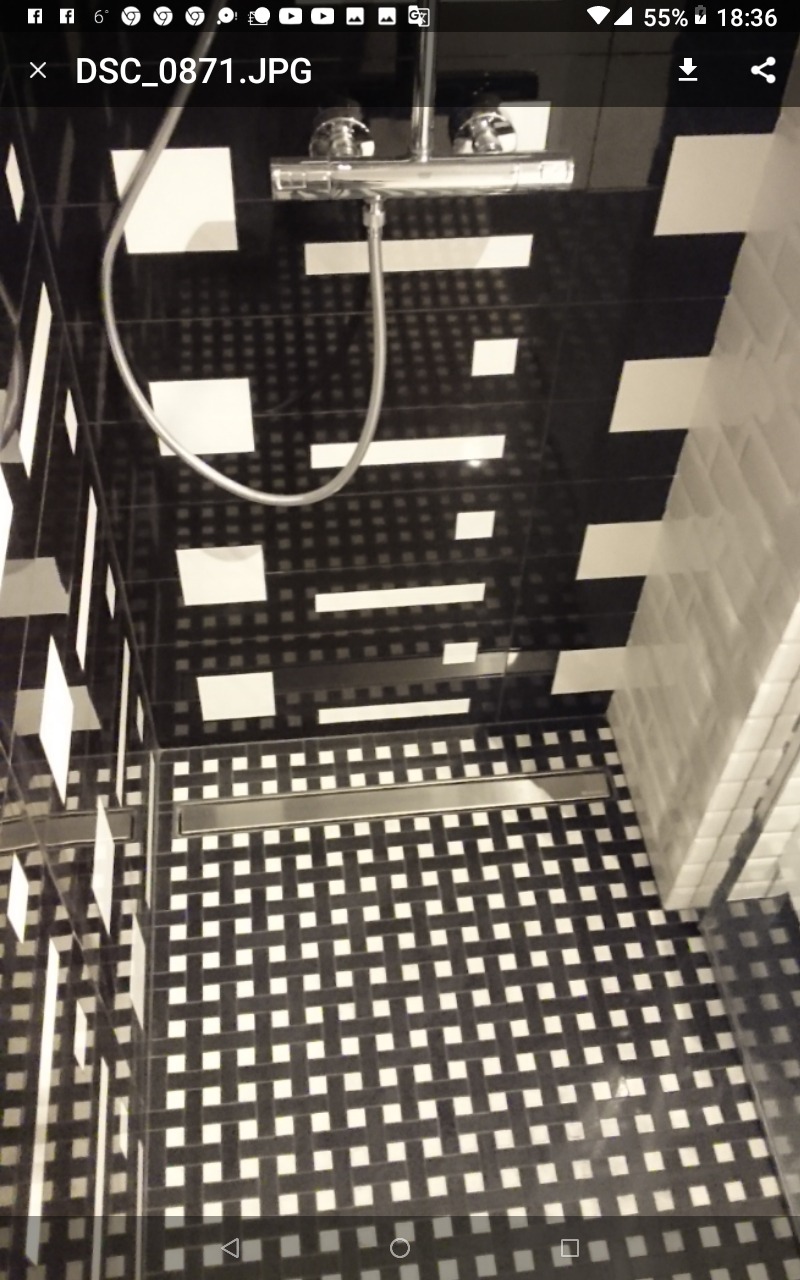 Kabina prysznicowa z czarno-białą mozaiką na podłodze i ścianach, chromowana bateria i odpływ liniowy.