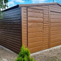 Brązowy garaż blaszany z dachem dwuspadowym, bramą uchylną po prawej i drzwiami wejściowymi po lewej stronie, wykończony w kolorze złotego dębu z poziomym profilem zamkniętym, ustawiony...