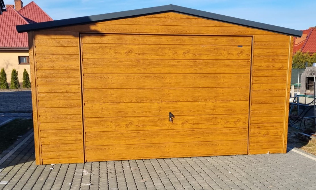 Nowoczesny, blaszany garaż z drewnopodobną fakturą w odcieniach brązu, z szarym dachem, umieszczony na kostce brukowej w słoneczny dzień.