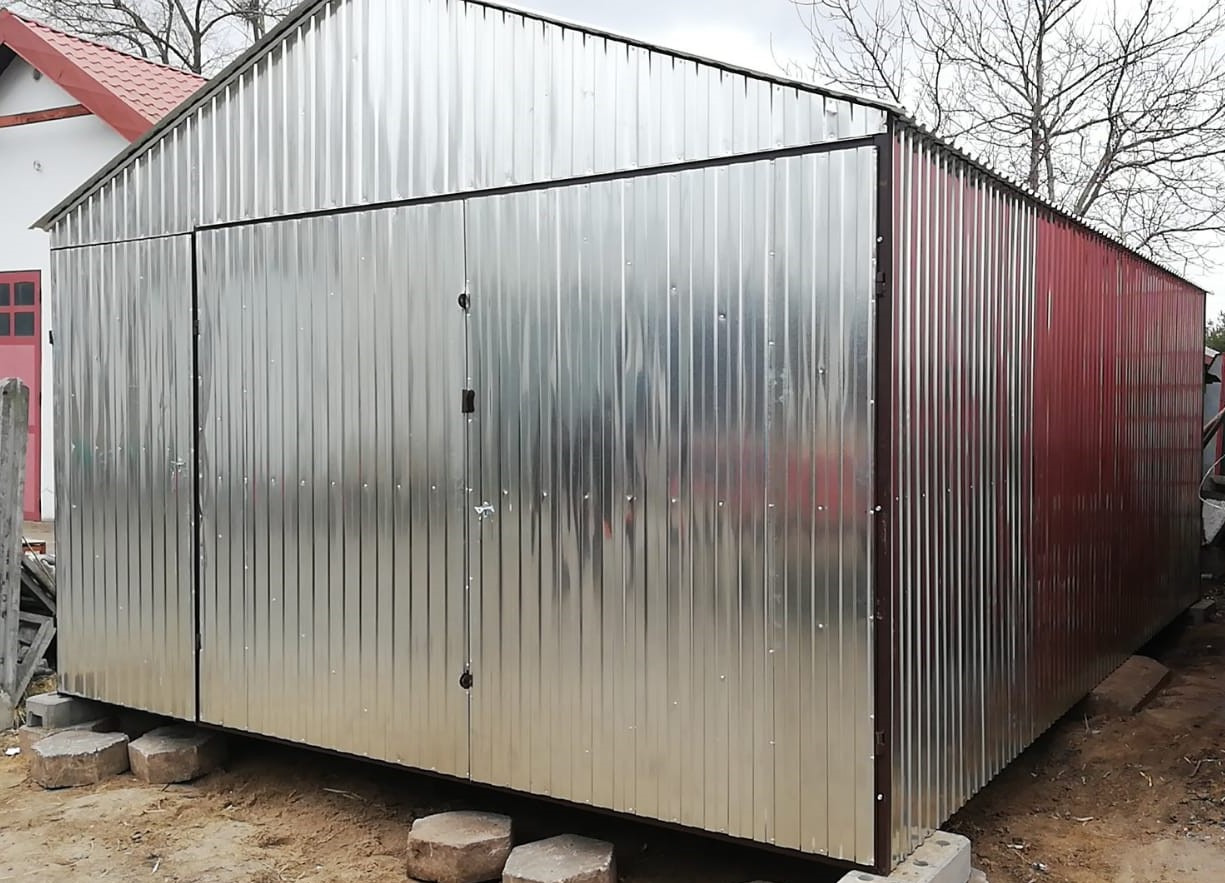 Gotowy garaż z blachy trapezowej, częściowo w kolorze srebrnym, częściowo w kolorze bordowym, posadowiony na betonowych bloczkach.