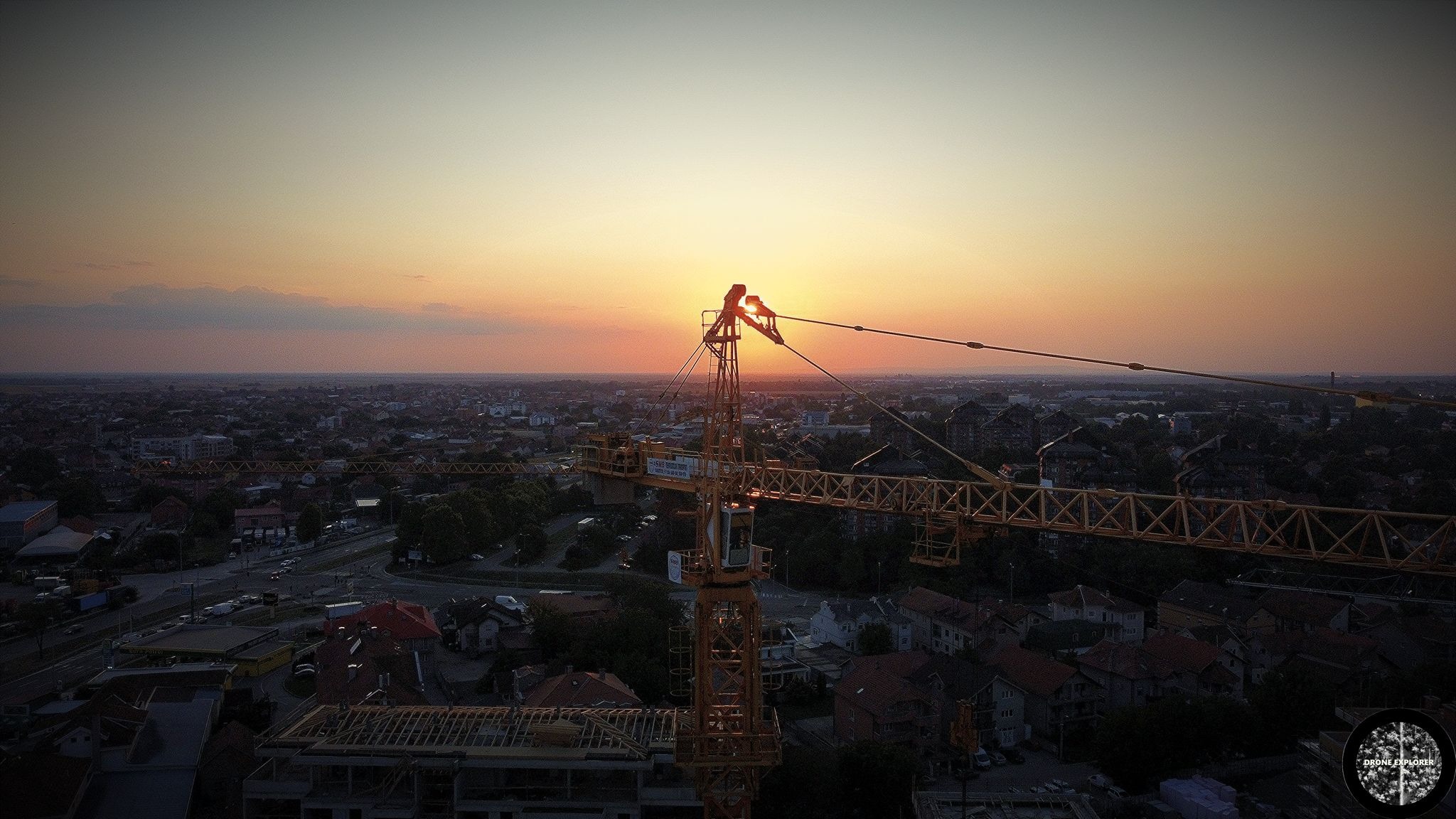 Żuraw budowlany na tle zachodzącego słońca i panoramy miasta, widok z lotu ptaka.