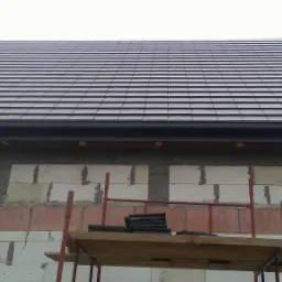 Nowy, ciemnoszary dach z dachówki ceramicznej, widok z rusztowania na budynek w trakcie budowy.