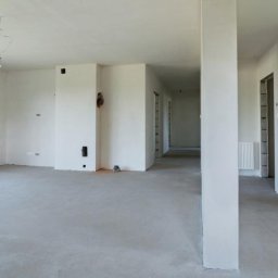 PrimaSort Remont - Surowe wnętrze domu w Zgierzu przed malowaniem, widoczne ściany po szpachlowaniu, surowy beton na podłodze, wystające kable i niedokończone gniazdka elektryczne.