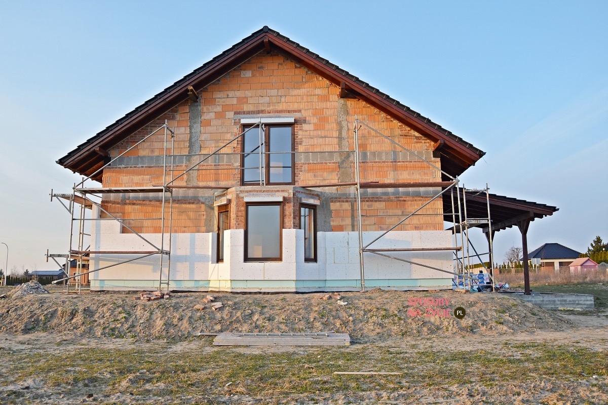 Dom jednorodzinny w trakcie ocieplania elewacji, widoczne rusztowania, styropian i pustaki ceramiczne.