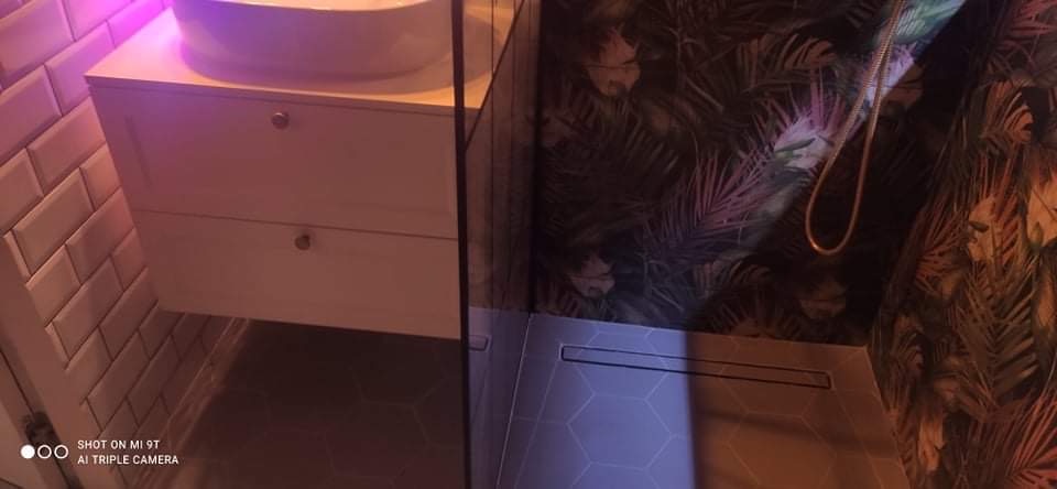 Nowoczesna łazienka z umywalką nablatową na szafce z dwiema szufladami, heksagonalną posadzką z odpływem liniowym i ścianą w tropikalne liście.