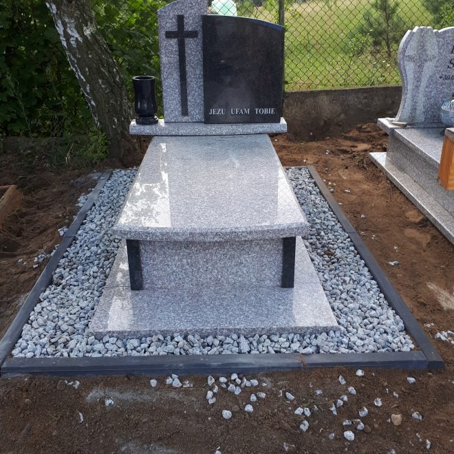 Jasnoszary pomnik z ciemnym napisem 'Jezu Ufam Tobie' i krzyżem, otoczony drobnymi kamykami i czarną obwódką.