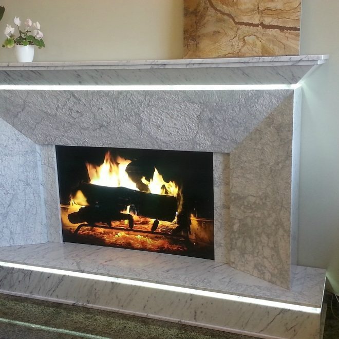 Marmurowy kominek z podświetleniem LED i płomieniami wewnątrz, wykonany w Turze. Na górze kominka stoi doniczka z kwiatami.