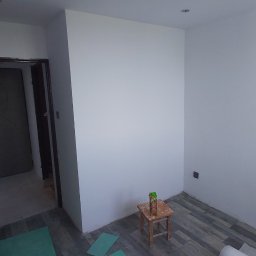 MagMarBud - Pokój po świeżym malowaniu, z otwartymi drzwiami, podłogą z paneli i stołkiem z sokiem w rogu, przygotowany do dalszych prac wykończeniowych.