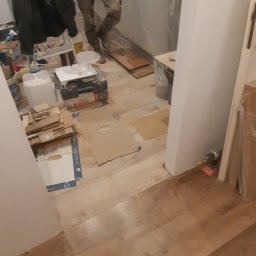 MagMarBud - Fragment wnętrza w trakcie prac wykończeniowych, widoczne ułożone panele podłogowe, narzędzia i materiały budowlane, w tle osoba w ubraniu roboczym.