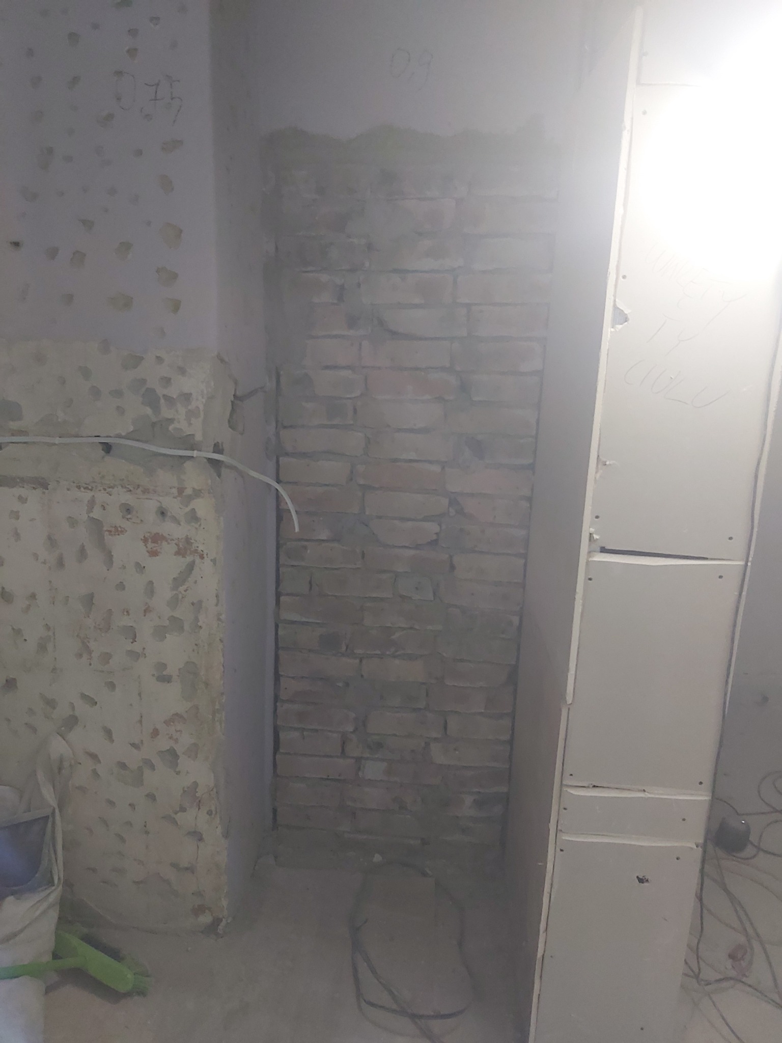 Wnęka z odsłoniętą cegłą, ściany w trakcie przygotowania do wykończenia, widoczne ślady po starej farbie i gładzi, obok płyty gipsowo-kartonowe.