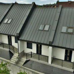 Nowoczesny szeregowiec z grafitowym dachem z blachy na rąbek stojący, oknami dachowymi i czarną stolarką okienną i drzwiową, widok z góry.