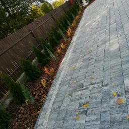 Nowo wybrukowana ścieżka z szarych płyt, obok kt&oacute;rej rosną małe, zielone drzewka iglaste i pomarańczowe krzewy, oddzielone od ścieżki korą.