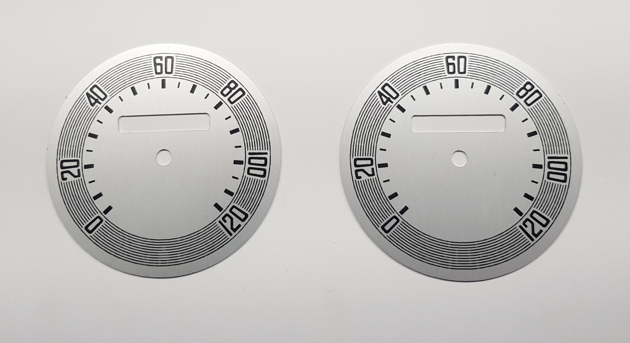Dwie srebrne tarcze prędkościomierza z czarnymi oznaczeniami, wyprodukowane w Łodzi, gotowe do montażu.