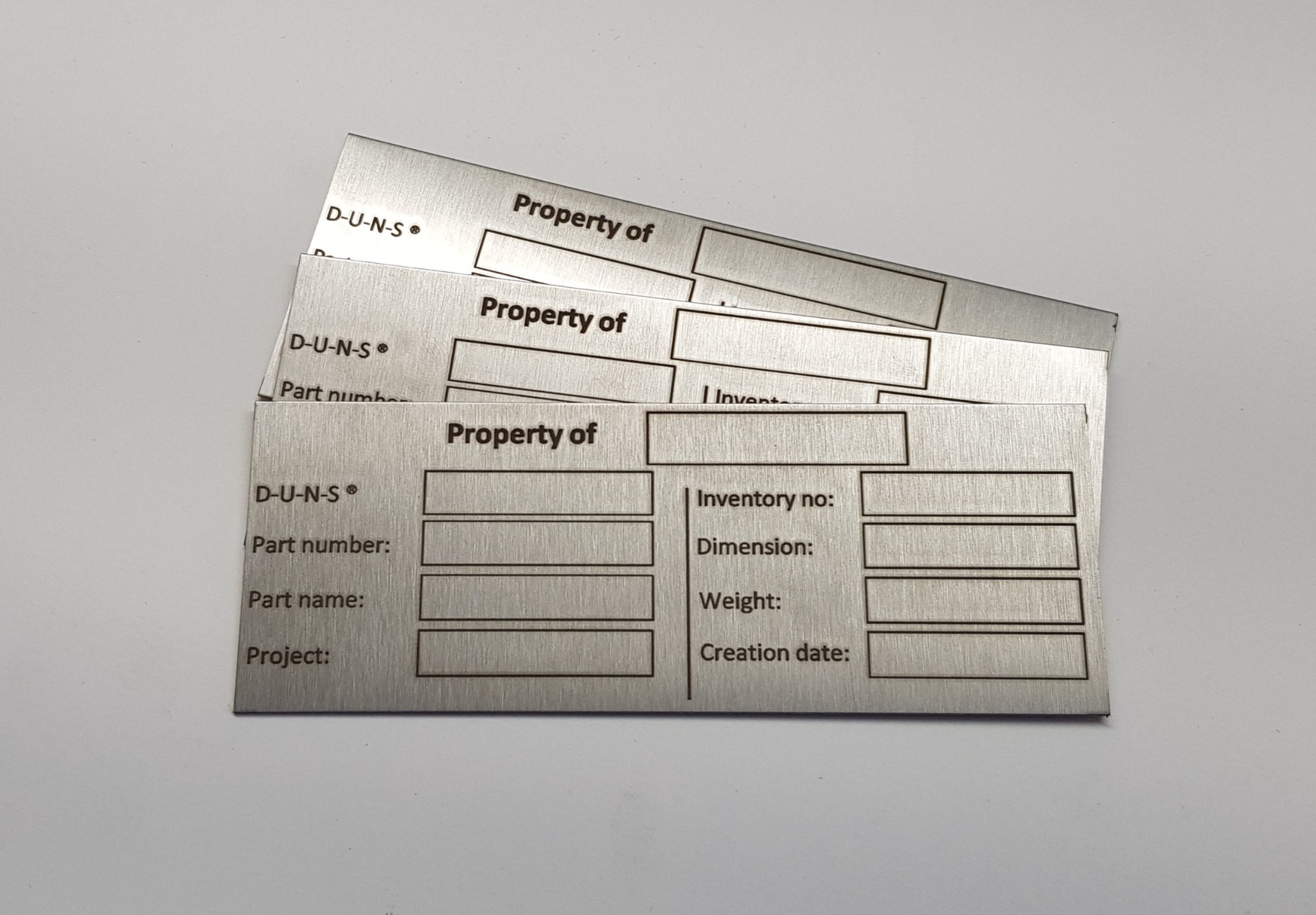 Metalowe tabliczki znamionowe z wygrawerowanymi danymi identyfikacyjnymi, takimi jak D-U-N-S, numer części, nazwa części, projekt, numer inwentarzowy, wymiary, waga i data utworzenia.
