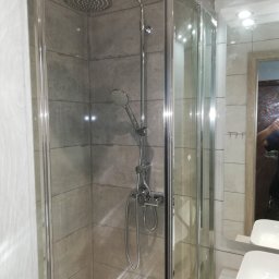 jacek nowak - Kabina prysznicowa z deszczownicą i baterią termostatyczną, wykończona szarymi płytkami imitującymi kamień, widoczne umywalki i fragment lustra.