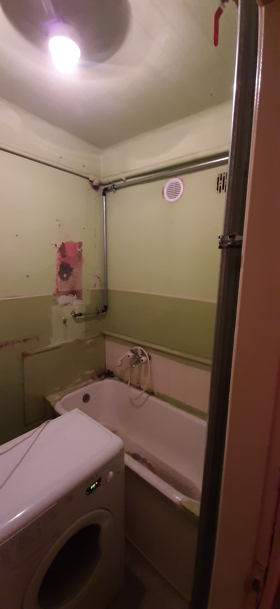 Łódź: Zaniedbana łazienka w trakcie przygotowań do remontu, widoczne ślady po usuniętych płytkach, stara wanna i pralka. Instalacja wodna na wierzchu.