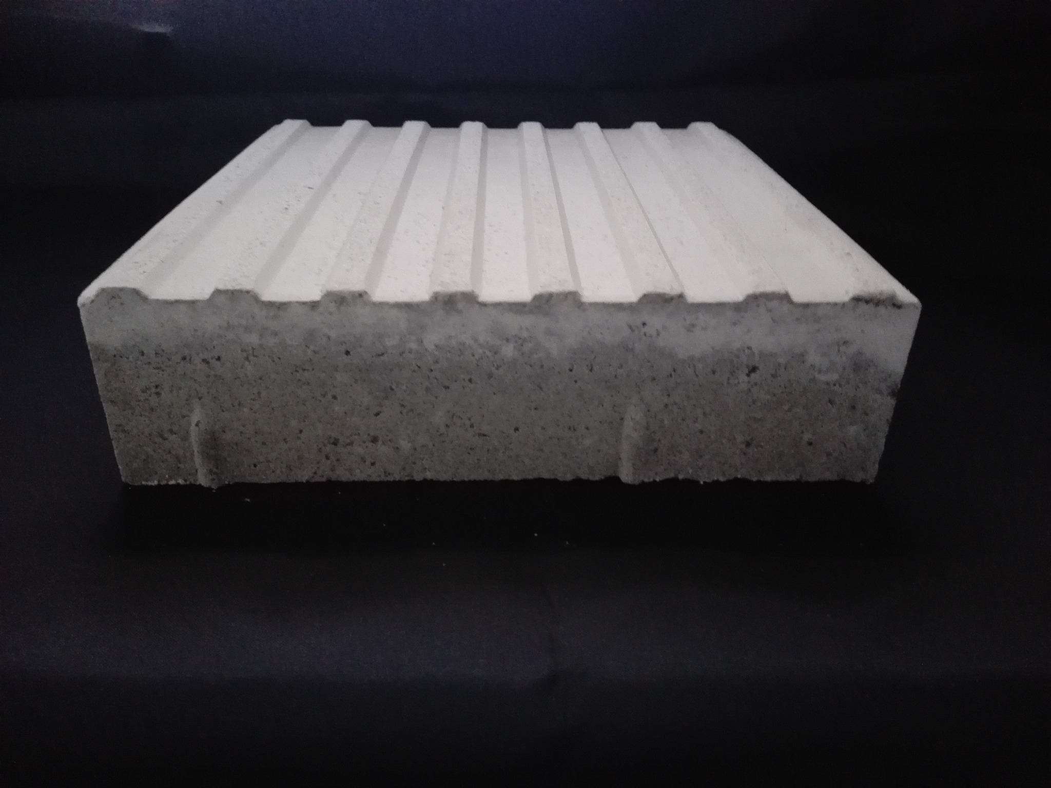 Betonowa płyta chodnikowa z rowkami na czarnym tle, widok z przodu, ukazujący strukturę betonu.