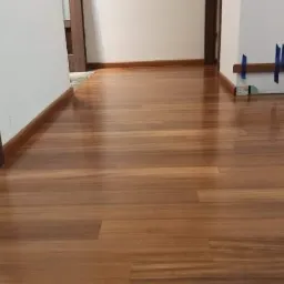 Świeżo ułożona, błyszcząca podłoga z paneli w odcieniach brązu, widoczne listwy przypodłogowe i fragmenty drzwi.