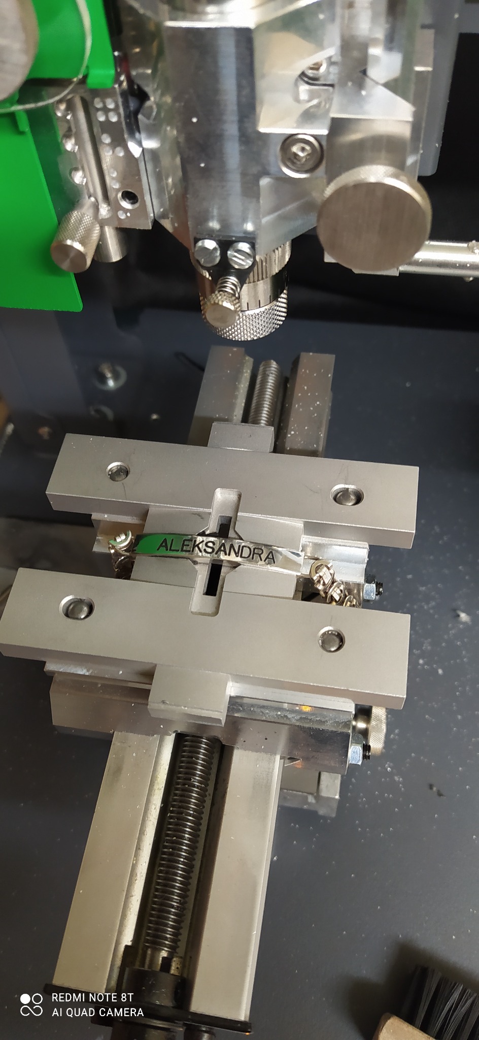 Proces grawerowania imienia 'Aleksandra' na metalowej bransoletce za pomocą precyzyjnej maszyny grawerującej.