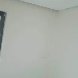 Świeżo pomalowane wnętrze pokoju z widocznym kablem zwisającym ze ściany i zabezpieczeniem podłogi taśmą malarską.