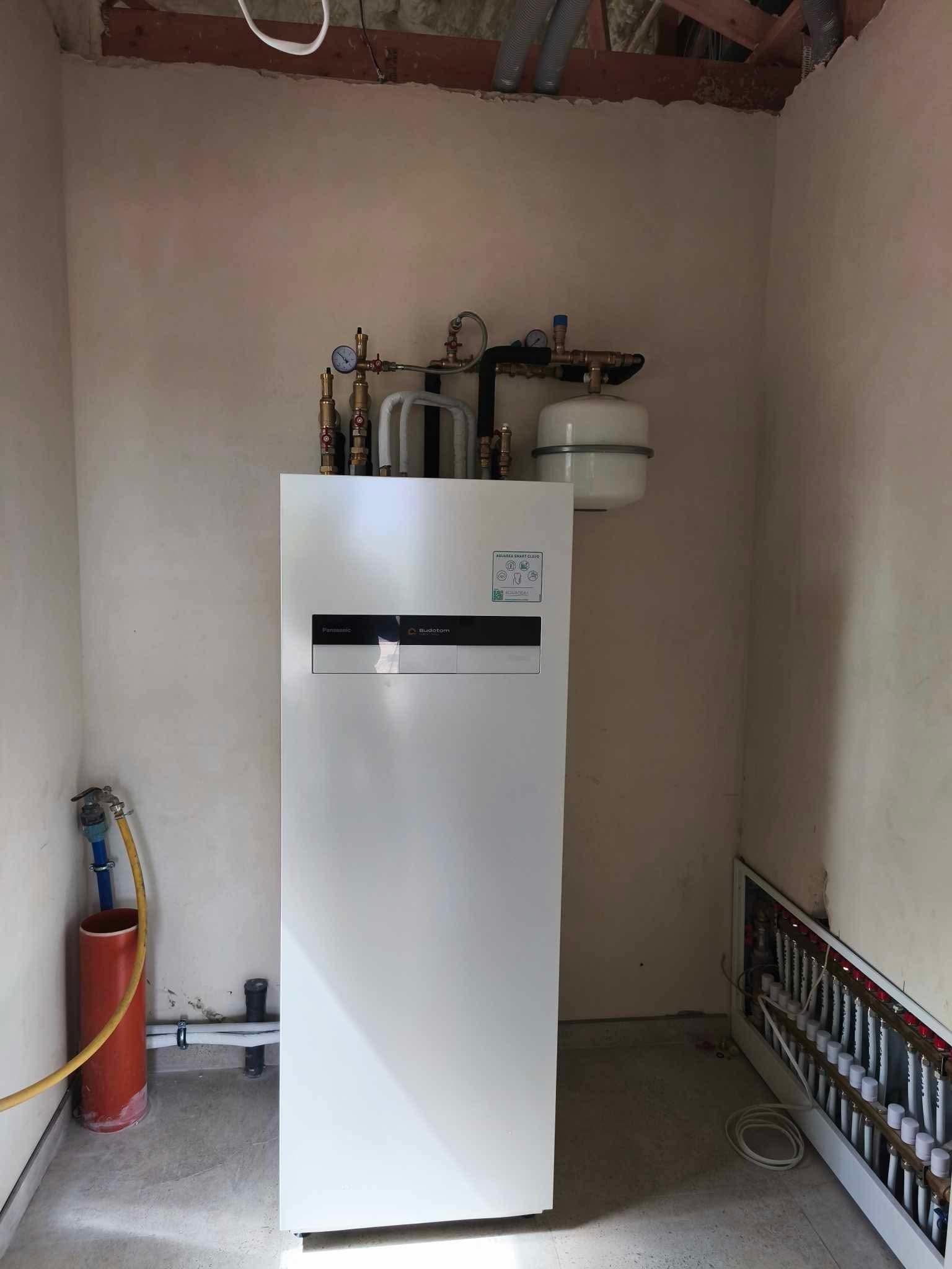 Biała pompa ciepła Buderus z instalacją hydrauliczną i rozdzielaczem ogrzewania podłogowego we Wrocławiu, widoczne rury pod sufitem i elementy montażowe.