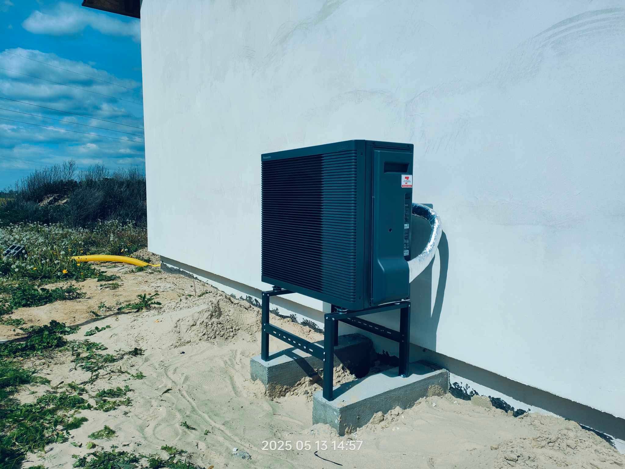 Nowoczesna pompa ciepła typu monoblok, zainstalowana na zewnątrz budynku na betonowym fundamencie. Widoczne przyłącza i fragment elewacji w surowym stanie.