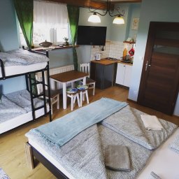 Przedsiębiorstwo Usługowe Komplex - Pokój wieloosobowy z łóżkiem piętrowym, podwójnym łóżkiem i aneksem kuchennym, oświetlony wiszącymi lampami i naturalnym światłem z okna z zielonymi zasłonami.