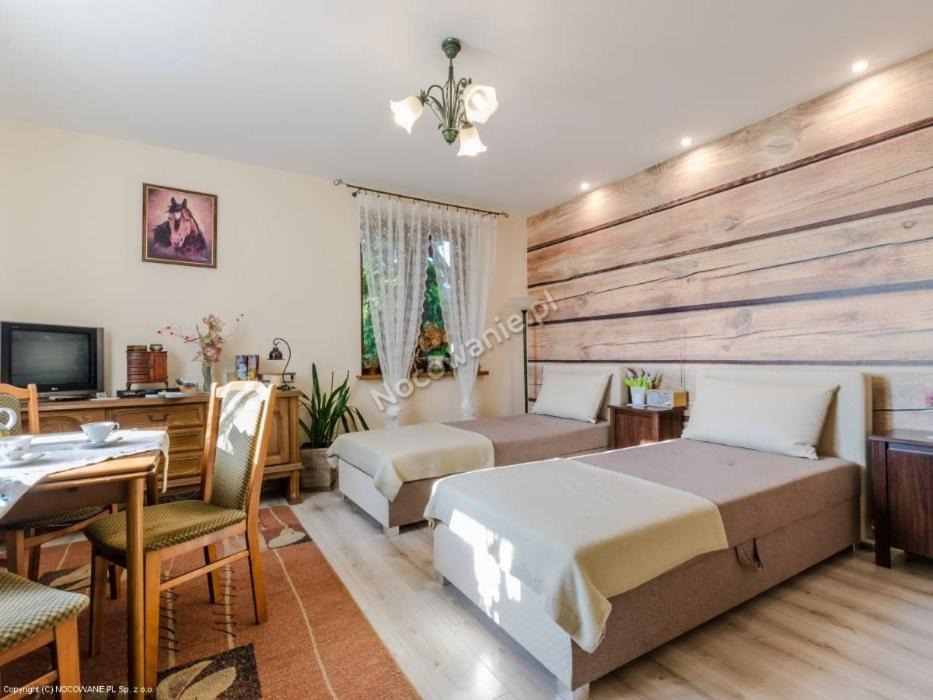 Pokój z dwoma pojedynczymi łóżkami, drewnianą ścianą, telewizorem i stołem z filiżankami, oświetlony żyrandolem.