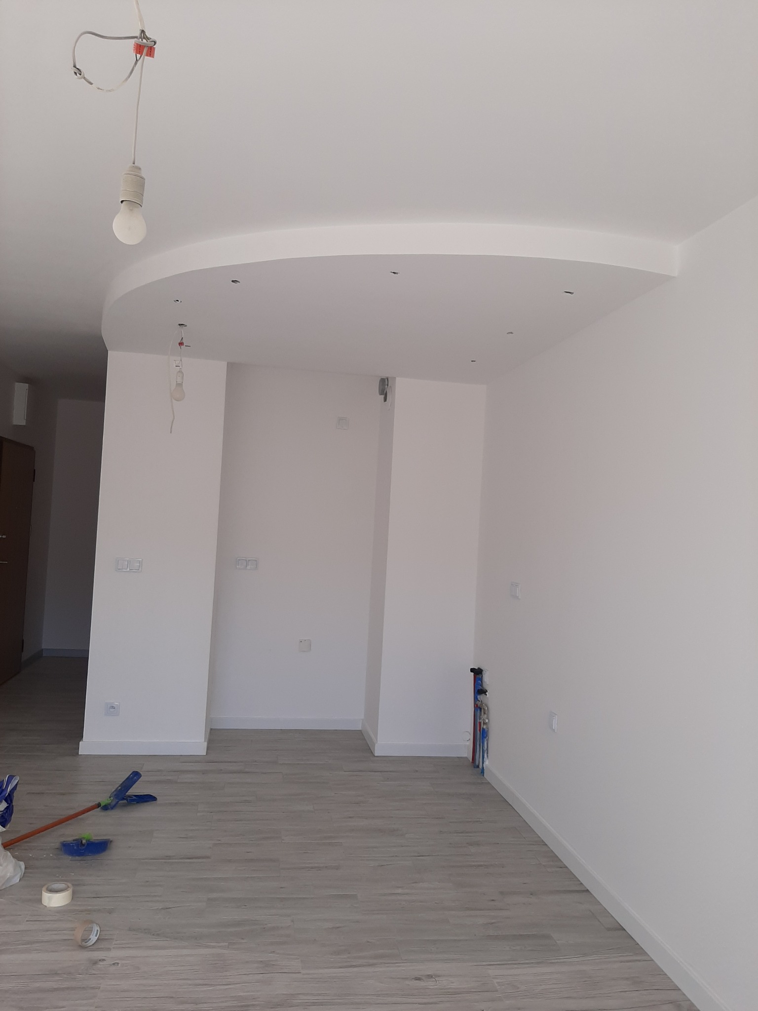 Wnętrze po malowaniu na biało, widoczne świeżo ułożone panele podłogowe, wystające kable oświetleniowe i narzędzia malarskie w rogu pomieszczenia.