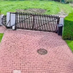 Automatyczna brama przesuwna z napędem, widok z góry na posesję z kostki brukowej i zadbaną zielenią.