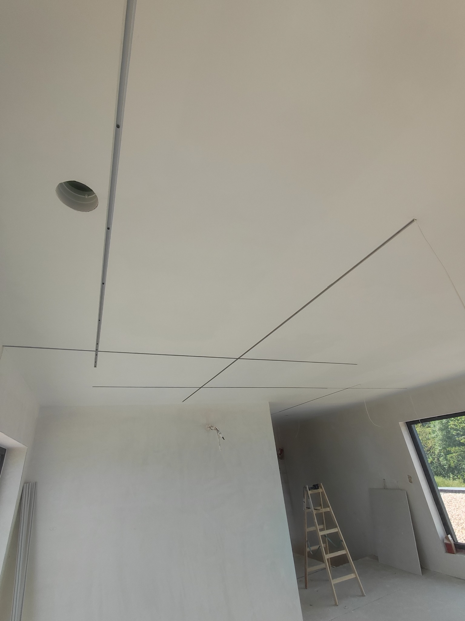 Montaż profili pod sufit napinany w jasnym pomieszczeniu, widoczna drabina i okno z widokiem na zieleń.