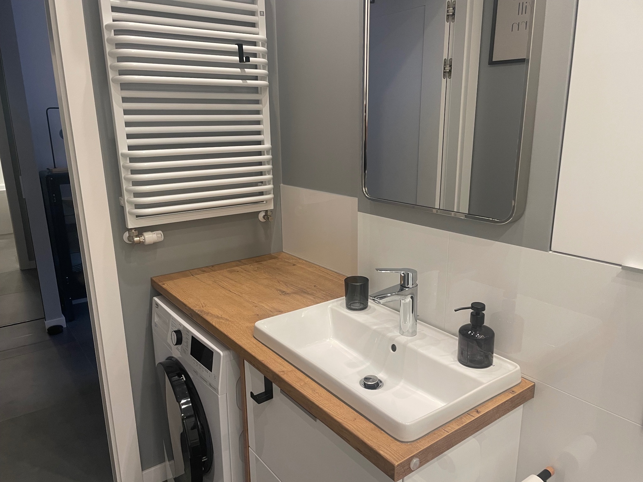 Nowoczesna łazienka z pralką pod blatem z umywalką, grzejnikiem drabinkowym i lustrem w metalowej ramie.