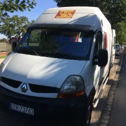 Biały Renault Master z logo firmy transportowej SJS na tle parku miejskiego, zaparkowany na ulicy, widoczna tablica rejestracyjna DTR 73763.