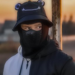 toporek_at_lens - Portret osoby w czarno-białej bluzie z kapturem, czarnym kapeluszu z uszkami i maską na twarzy, stojącej obok metalowego słupka na rozmytym tle o zachodzie słońca.