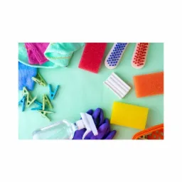 Zestaw kolorowych akcesoriów do sprzątania w Łodzi: ściereczki, gąbki, szczotki, klamerki i butelka ze spryskiwaczem, ułożone na jasnym tle.