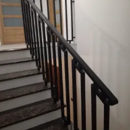 Metalowa balustrada schodowa w kolorze czarnym, z geometrycznym wzorem, zamontowana na schodach z ciemnego granitu, widok z dołu