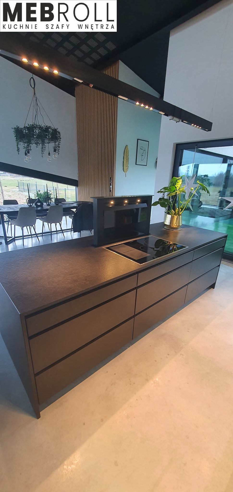 Nowoczesna, grafitowa wyspa kuchenna z płytą indukcyjną i pochłaniaczem w minimalistycznym wnętrzu z drewnianymi lamelami i widokiem na zieleń za oknem.