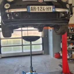 Czarny Fiat 500 na podnośniku warsztatowym podczas wymiany oleju, widoczny zbiornik na zużyty olej marki GEKO, tablica rejestracyjna AR-124-HY.