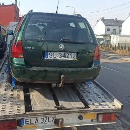 Zielony Volkswagen Bora kombi zabezpieczony niebieskimi pasami na platformie lawety, widok z tyłu, tablica rejestracyjna SL 34212, w tle zabudowa miejska.