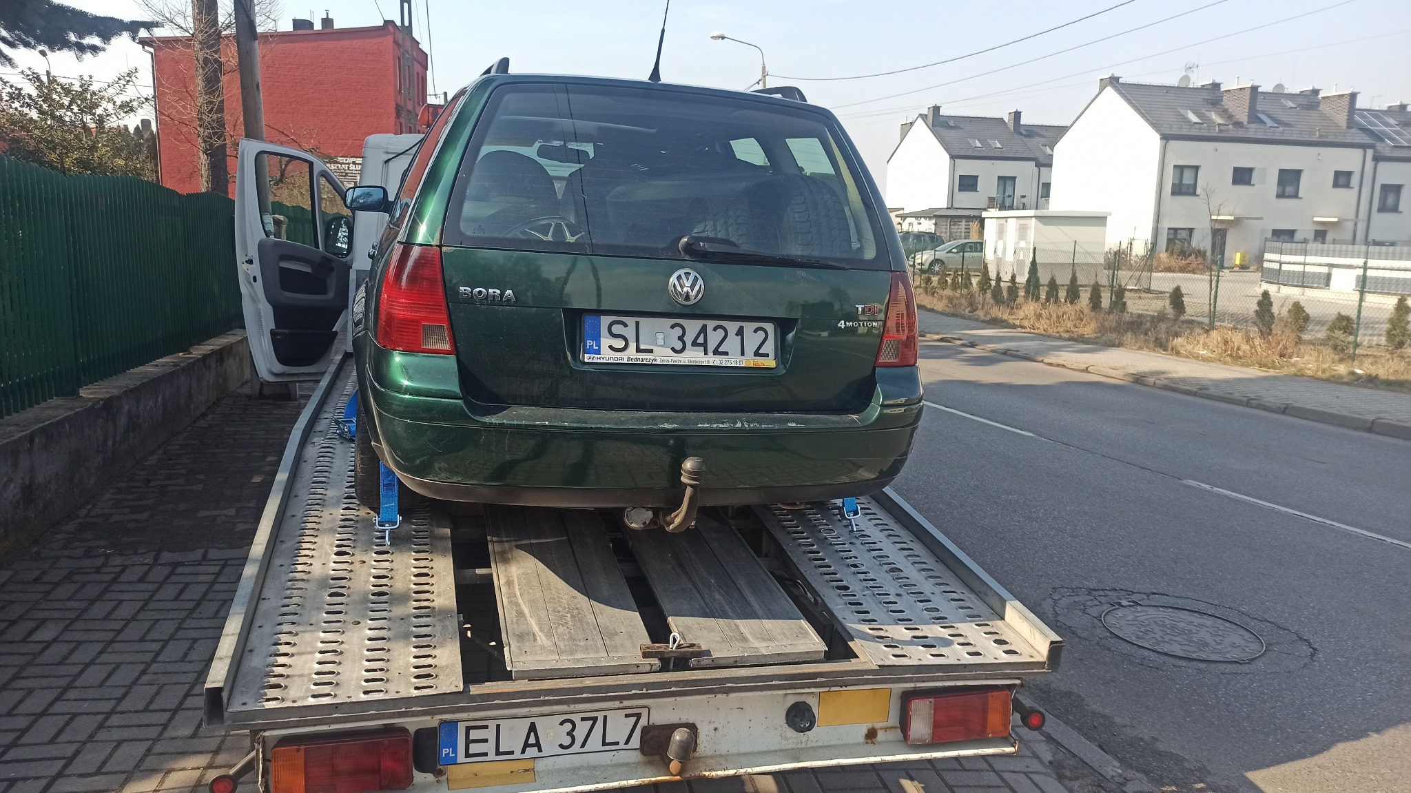 Zielony Volkswagen Bora kombi zabezpieczony niebieskimi pasami na platformie lawety, widok z tyłu, tablica rejestracyjna SL 34212, w tle zabudowa miejska.