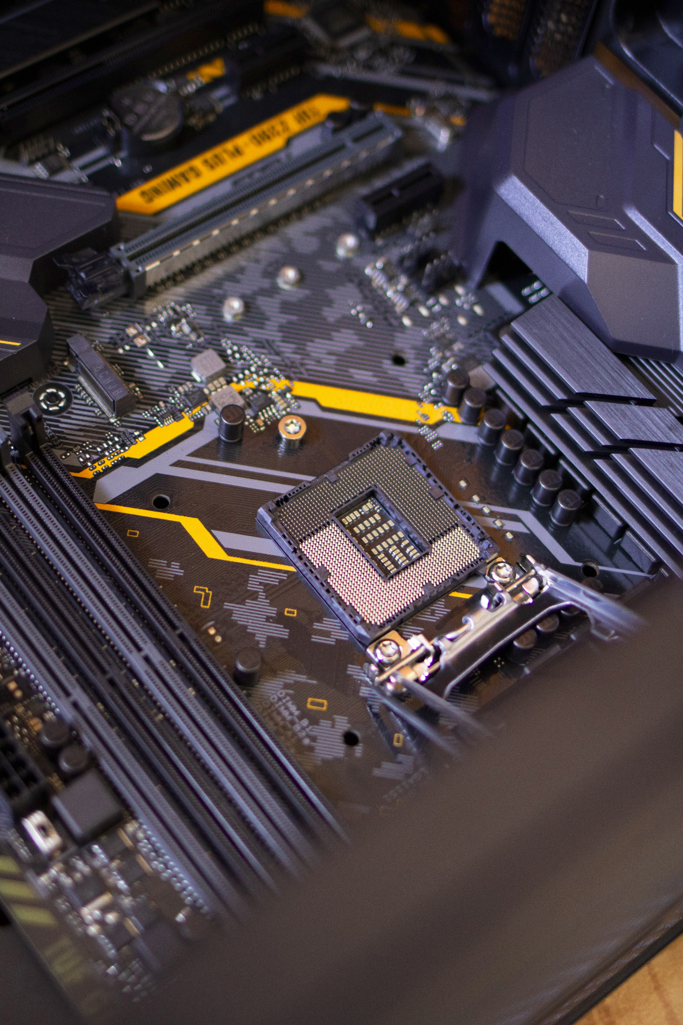 Detalistyczny widok płyty głównej komputera z gniazdem procesora, elementami zasilania i slotami pamięci RAM, z akcentami w kolorze żółtym.