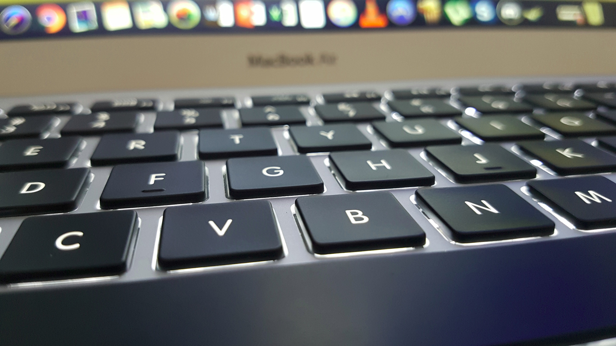 Zbliżenie na podświetlaną klawiaturę laptopa Macbook Air z widocznymi ikonami aplikacji na górnym pasku ekranu.