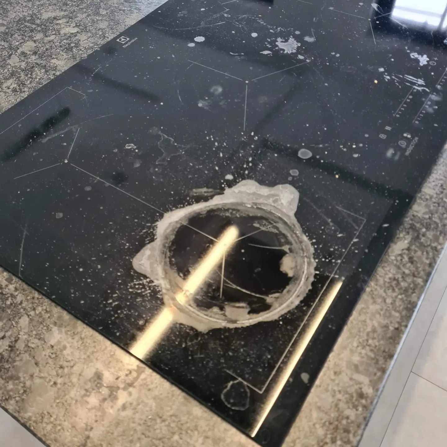 Zabrudzona płyta indukcyjna Electrolux pokryta zaschniętymi plamami i resztkami jedzenia, widoczne ślady po czyszczeniu w jednym z rogów.