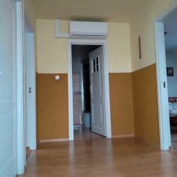 NOVO-TECH Sławomir Czmiel - Korytarz z widocznym klimatyzatorem nad drzwiami do łazienki, ściany w kolorze żółtym i brązowym, parkiet na podłodze.