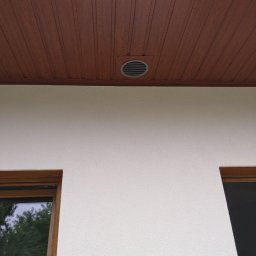 NOVO-TECH Sławomir Czmiel - Elewacja budynku z widocznym otworem wentylacyjnym pod drewnianą podbitką dachową, obok fragmenty okien.