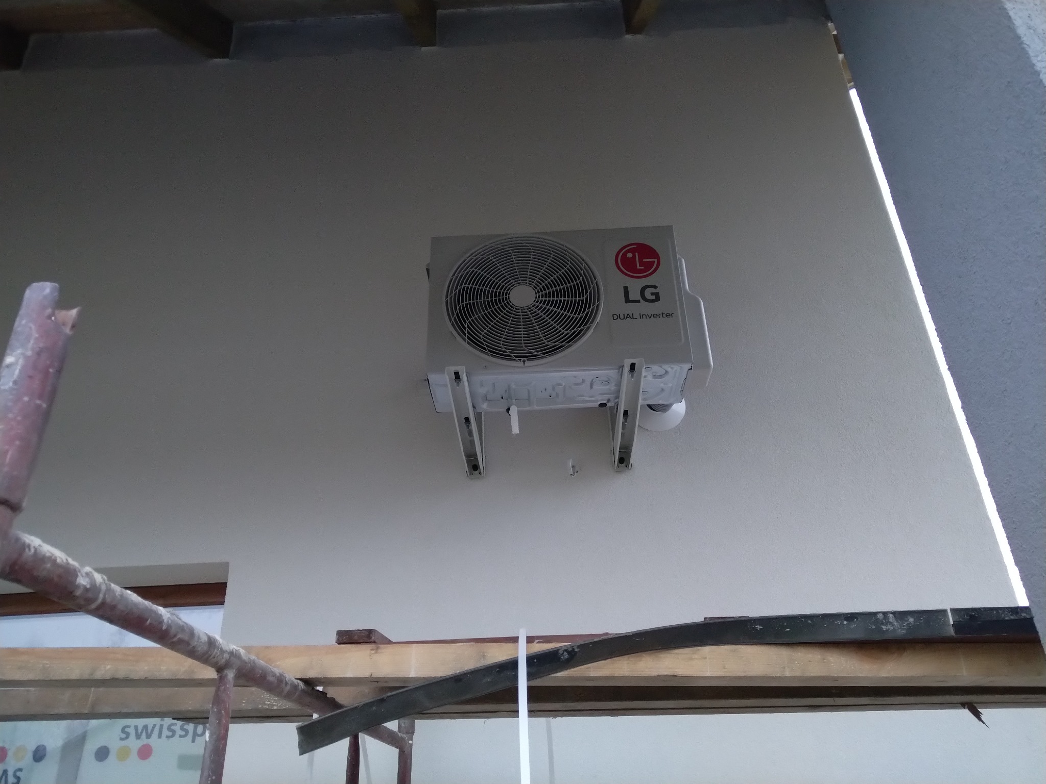 Zewnętrzna jednostka klimatyzacji LG Dual Inverter zamontowana na ścianie budynku, widoczne rusztowanie w dolnej części kadru.