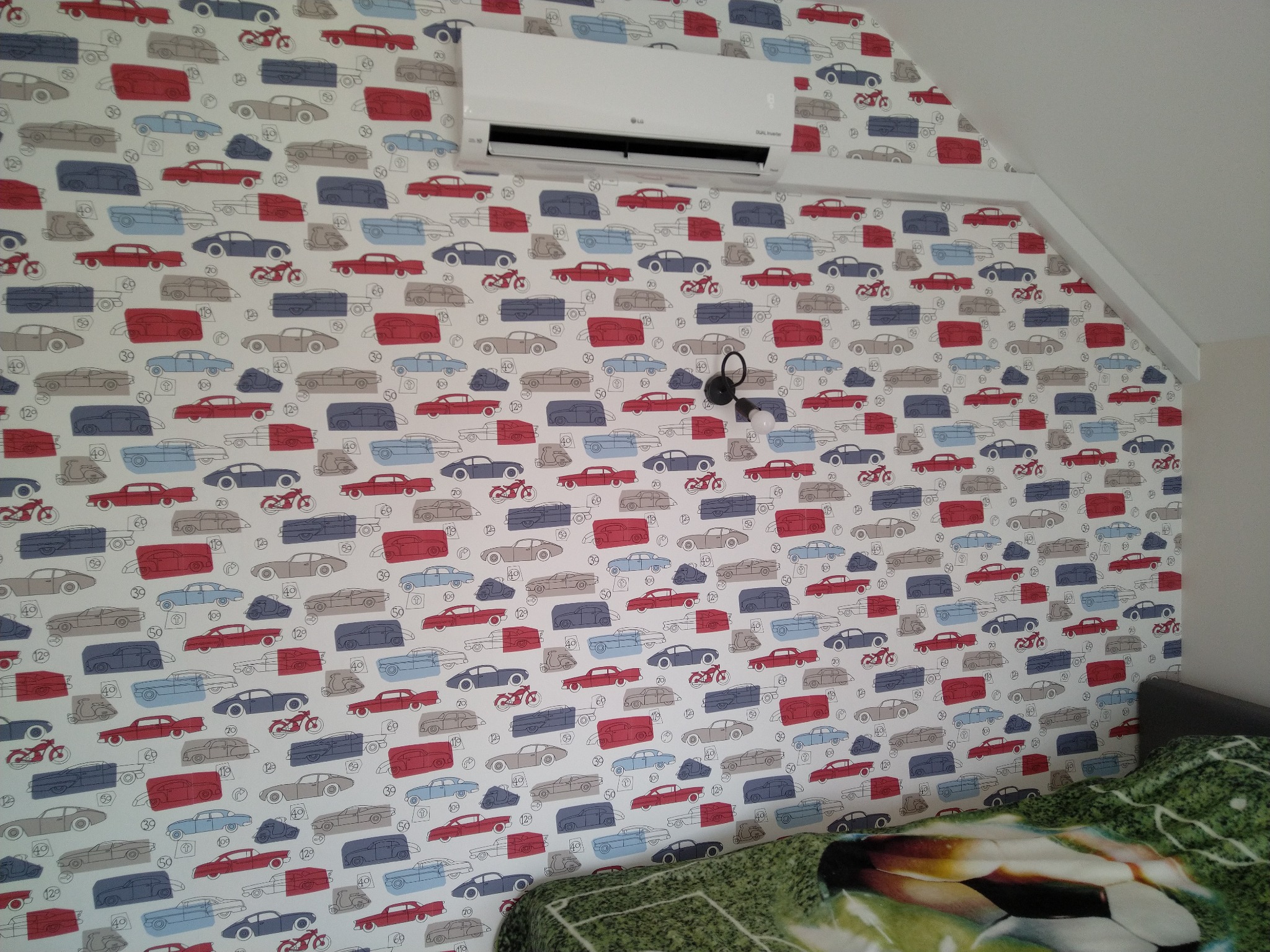 Biały klimatyzator LG zamontowany na ścianie z tapetą w kolorowe samochody i motocykle w pokoju na poddaszu.