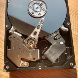 Otwarty dysk twardy na drewnianym stole, widoczne talerze, głowice i mechanika wewnętrzna, oświetlone naturalnym światłem.