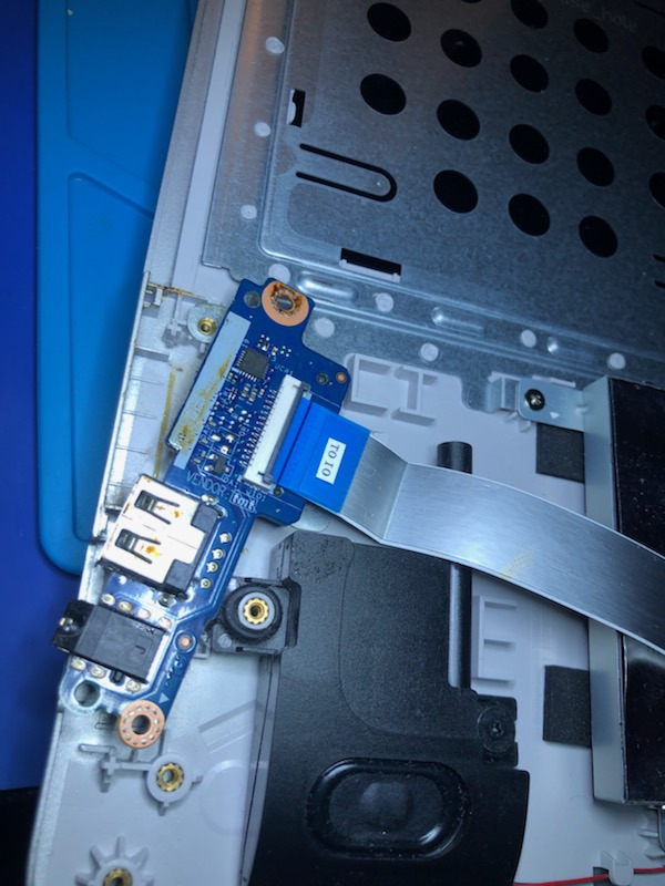 Wnętrze laptopa z widoczną płytką z portami USB i audio, połączoną taśmą do płyty głównej, podczas demontażu lub naprawy.