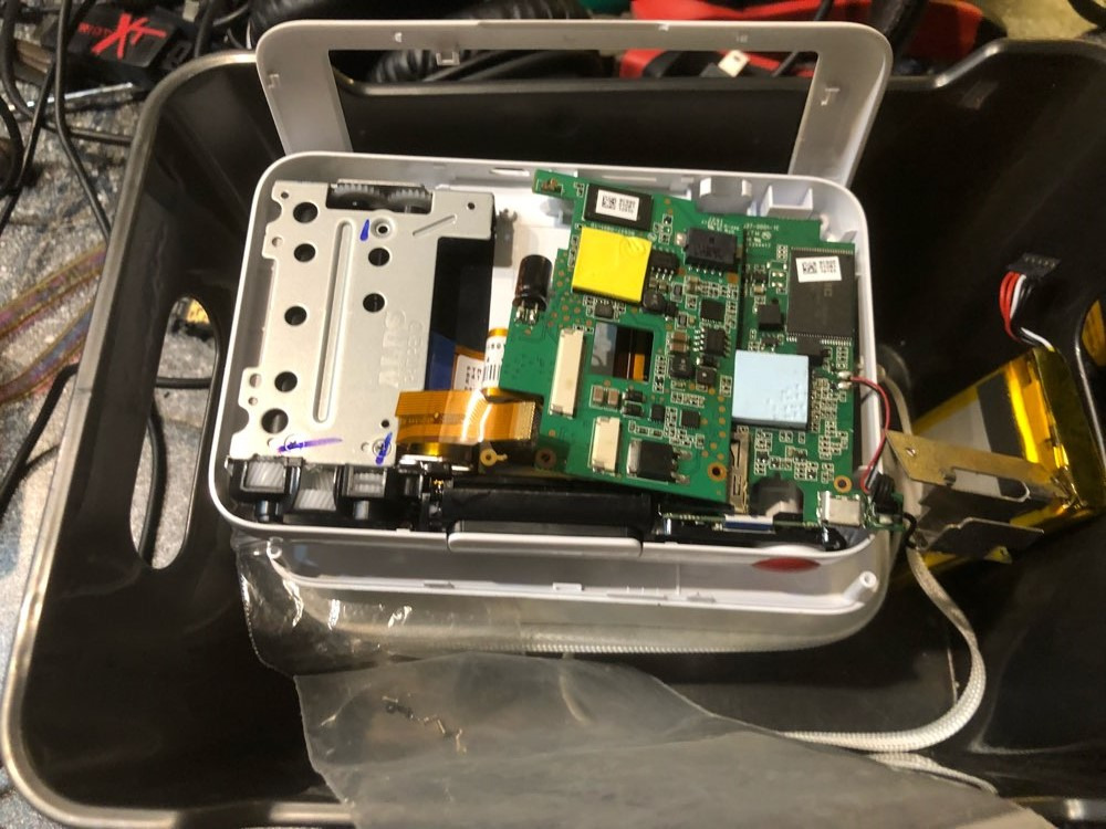 Wnętrze rozłożonego urządzenia elektronicznego z widoczną płytą główną, baterią i elementami mechanicznymi, umieszczone w plastikowej kuwecie.